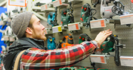 Handwerker im Baumarkt vor einer Regalwand mit Stichsägen zum Kauf